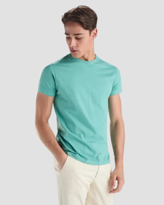 Man wearing a teal t-shirt and white pants on a light gray background