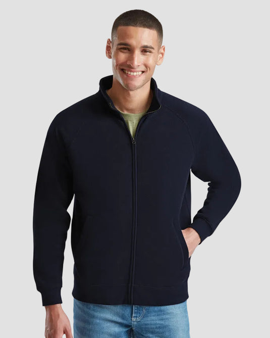 A man wearing a navy blue zip-up fleece jacket over a light green t-shirt and blue jeans, standing against a solid gray background.