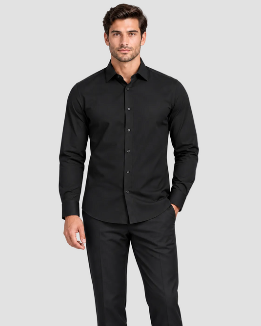 A man modeling a black long-sleeve button-down dress shirt with matching black trousers, standing against a solid light gray studio background.