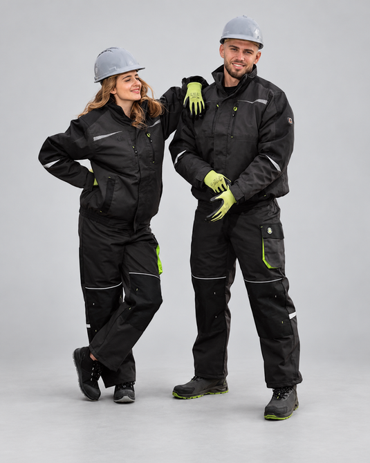 A man and a woman modeling matching black workwear sets with high-visibility lime green gloves and helmets, standing against a neutral gray studio background.