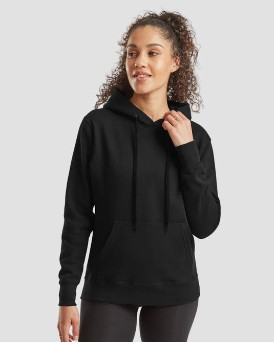 A woman wearing a black pullover hoodie with drawstrings and a front kangaroo pocket, paired with black fitted shorts, against a light gray studio background.