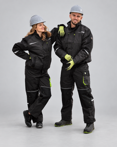 A man and a woman modeling matching black workwear sets with high-visibility lime green gloves and helmets, standing against a neutral gray studio background.