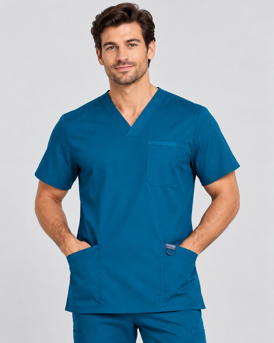 A man wearing a teal blue V-neck scrub top and matching scrub pants, standing against a light gray studio background.