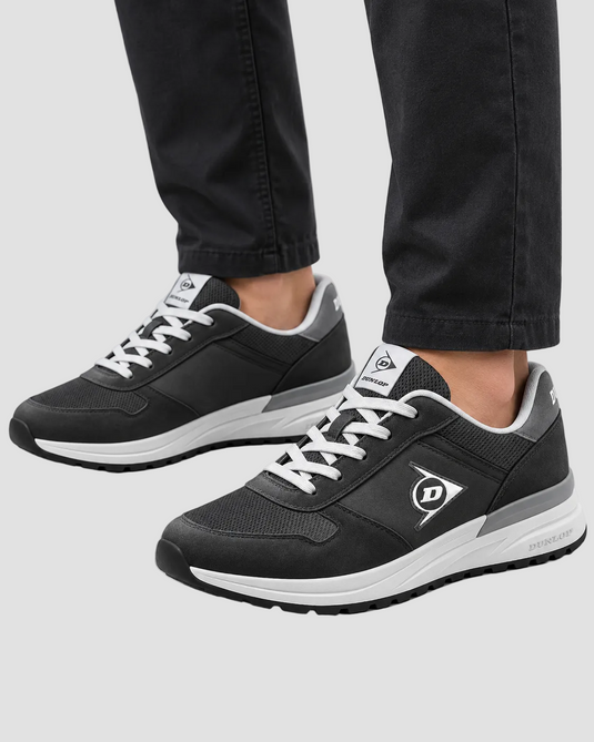 A pair of black and white Dunhill sneakers worn with black jeans, shown from a side angle against a light gray studio background.